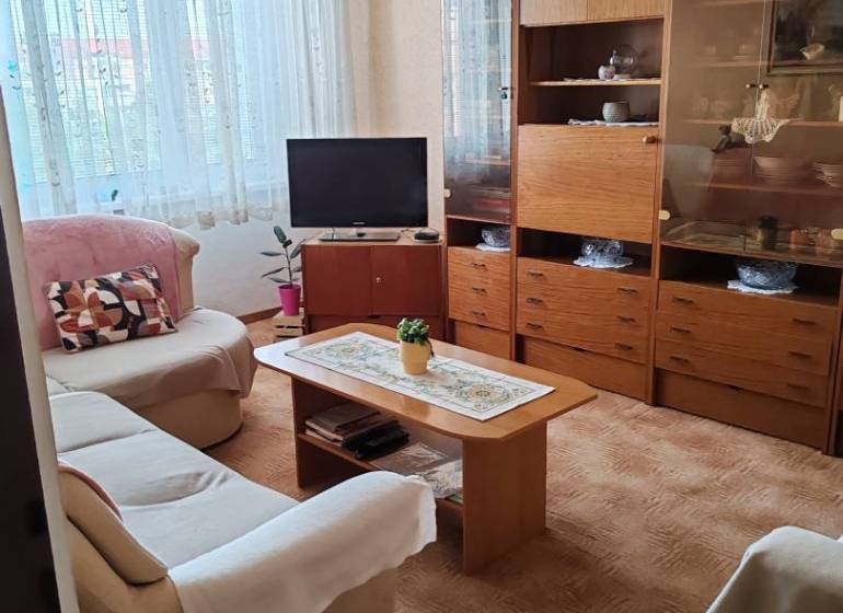 Nappali kanapéval, televízióval és fa szekrénnyel egy háromszobás lakásban.