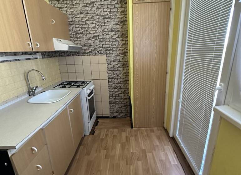 Konyha fa szekrényekkel, tűzhellyel és mosogatóval egy egyszobás lakásban.