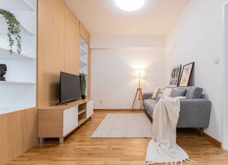 Nappali TV-vel, szürke kanapéval és dekorációs elemekkel egy háromszobás lakásban.