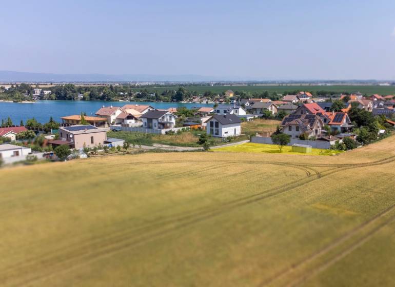 Telkek - lakóövezet Dunajská Lužná-ban, kilátással a tóra, házak és mező.