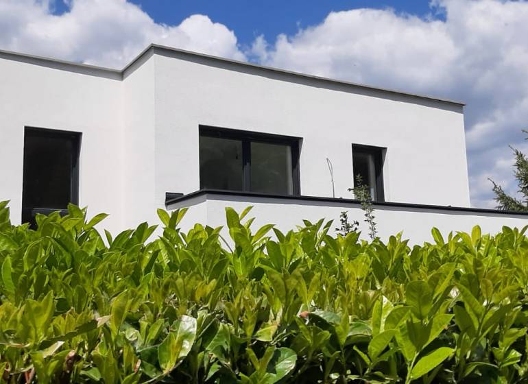Fehér homlokzatú villa Hainburg an der Donau-ban, zölddel körülvéve a kék ég alatt.