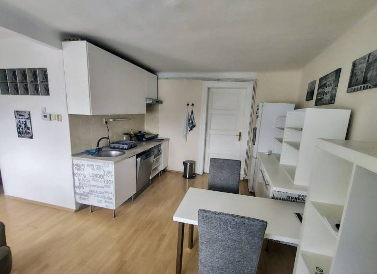 Konyha egy kétszobás lakásban étkezőasztallal, fehér szekrényekkel és fa padlóval.