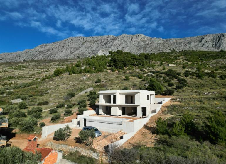 Villa Duće zölddel és hegyekkel körülvéve, háttérben kék ég.