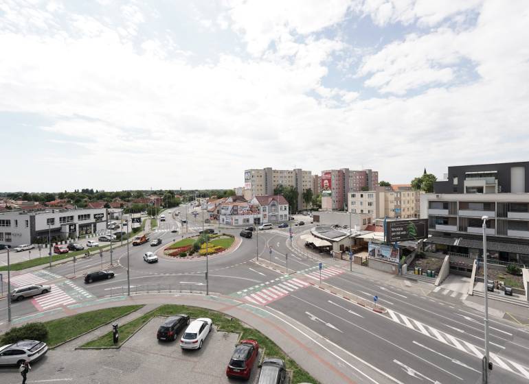 Körforgalom és környezete a Fő utcán Dunaszerdahelyen, autók mozgása, épületek, égbolt.