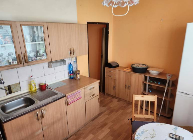 Konyha egy egyszobás lakásban fa szekrényekkel, asztallal és hűtőszekrénnyel.