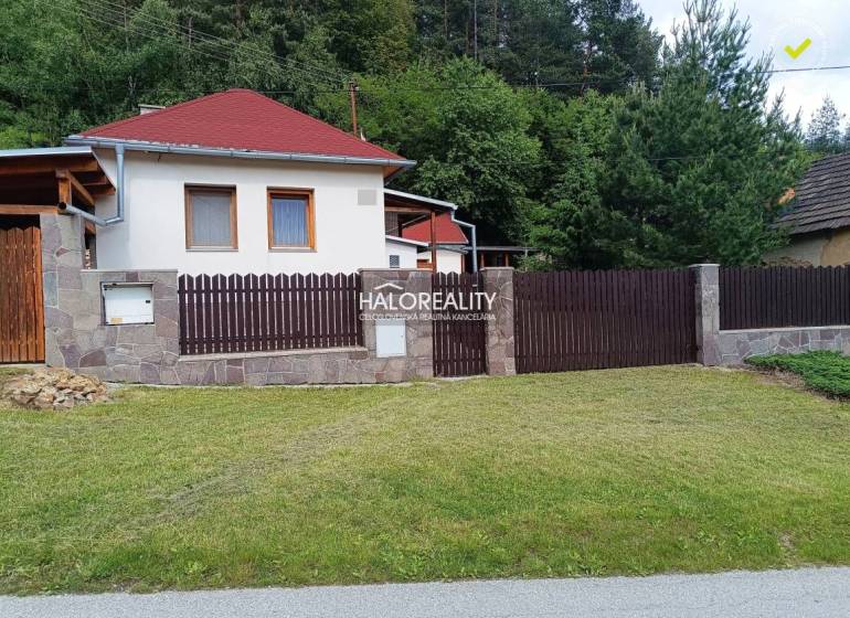 Egy helcmanovcei ház fa kerítéssel és rendezett gyepfelülettel, zöld növényzettel körülvéve.