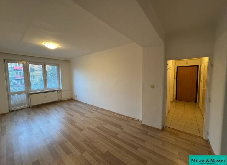 Tágas szoba laminált padlóval egy 2 szobás lakásban, napfény árad be a nagy ablakon keresztül.