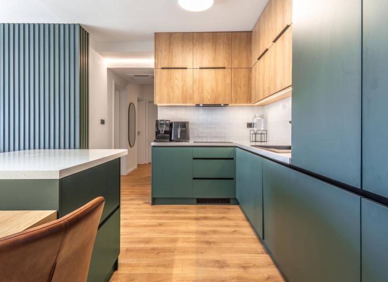 Konyha egy háromszobás lakásban, fa dekor padlóval és zöld szekrényekkel.