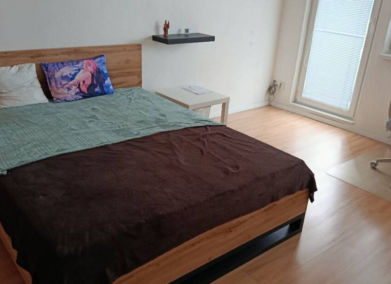 Hálószoba egy egyszobás lakásban fa dekor padlóval, ággyal és irodai székkel.