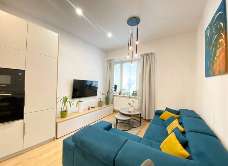 Nappali egy kétszobás lakásban kék kanapéval és fa mintázatú padlóval.