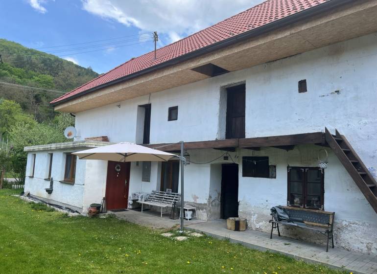 Vidéki ház piros tetővel és terasszal, zöld gyep és természet veszi körül.