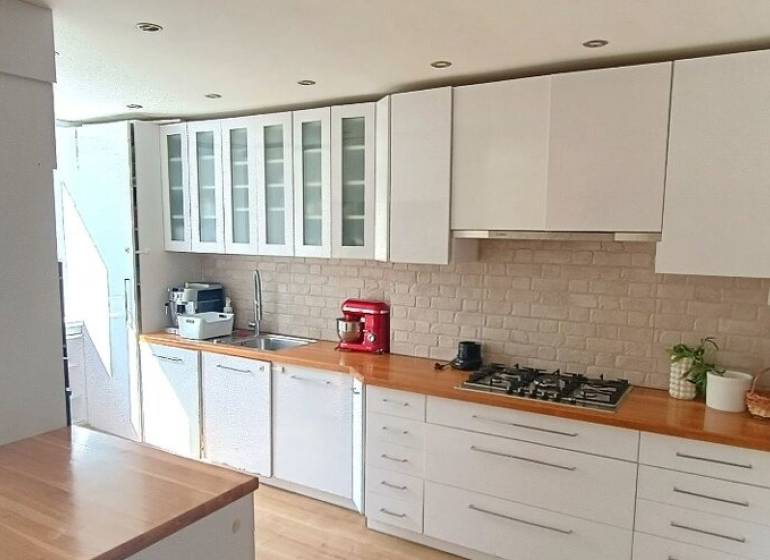 Konyha egy háromszobás lakásban fehér bútorokkal és tűzhellyel, fa dekoros padlóval.