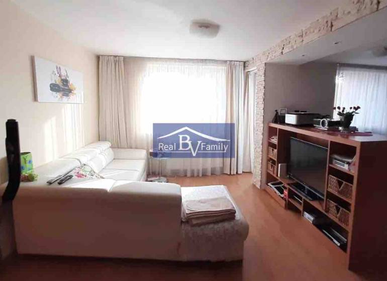 Nappali fehér kanapéval és televízióval, fa hatású padlóval, 2 szobás lakás.