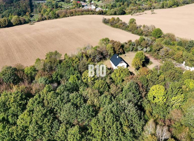 Ház Lackovban, erdővel és mezőkkel körülvéve, nyugodt vidéki táj.