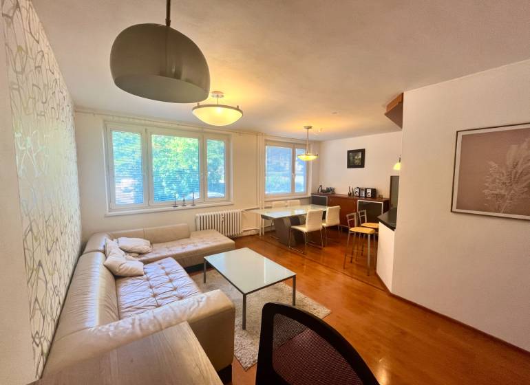 Nappali egy háromszobás lakásban kanapéval, asztallal és étkező sarokkal.