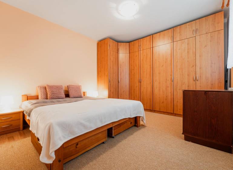 Hálószoba egy háromszobás lakásban ággyal, beépített szekrénnyel és fa dekorációjú padlóval.