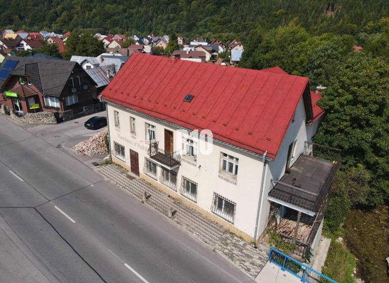 Az épület Bélán piros tetővel, környező házak és természet.