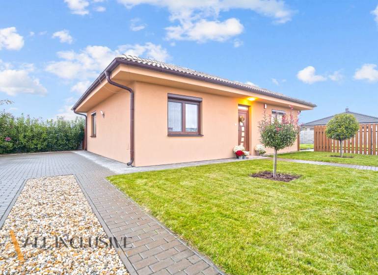 Családi ház Bősön, amelyet zöld növényzet, térkő és egy kis fa vesz körül a kertben.