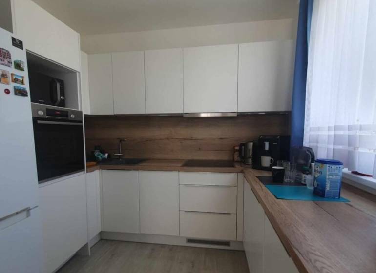 Konyha fehér szekrényekkel, fa dekorációval a padlón és munkalapon egy kétszobás lakásban.