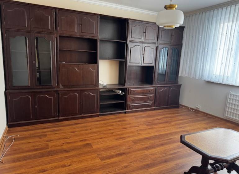 Nappali egy háromszobás lakásban, fa dekor padlóval, sötét bútorokkal.