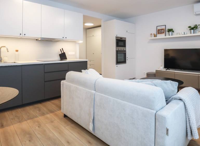 Nappali egy egyszobás lakásban konyhabútorral, kanapéval és fa dekor padlóval.