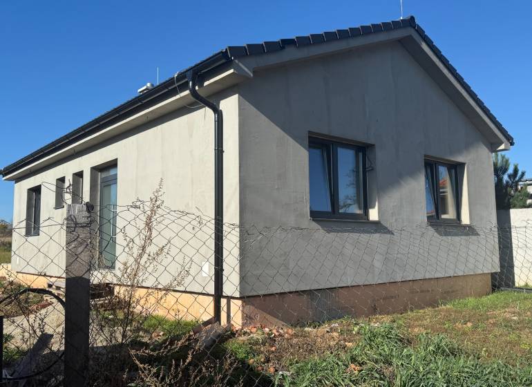 Családi ház Tesárske Mlyňany-ban szürke homlokzattal és ablakokkal, kerítéshálóval körbekerítve.