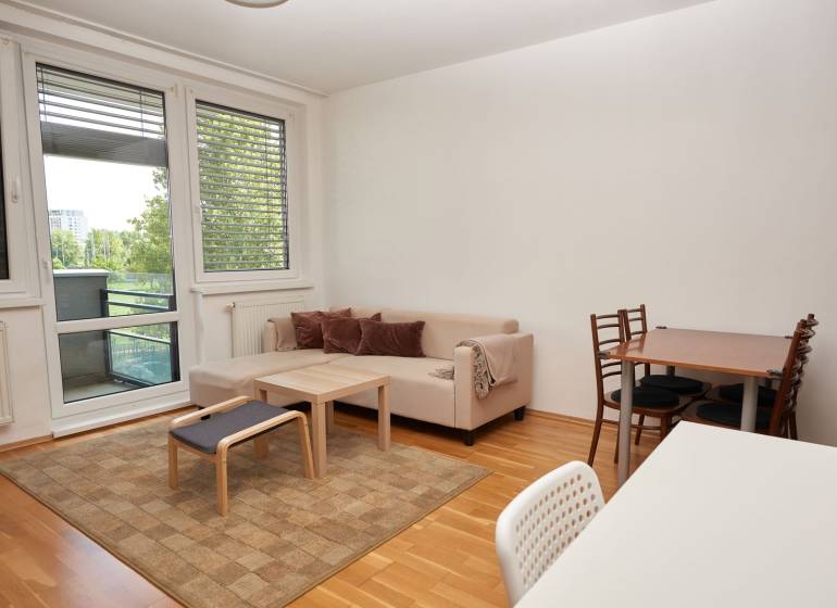 Nappali kanapéval, étkezőasztallal és fa dekorációjú padlóval egy kétszobás lakásban.