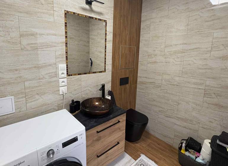 Fürdőszoba kerámia mosdóval és mosógéppel egy kétszobás lakásban, fa dekoros padlóval.