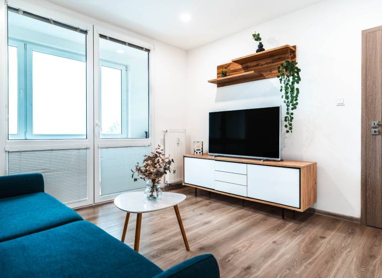 Nappali egy kétszobás lakásban kanapéval, televízióval és fa dekorációjú padlóval.