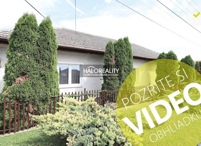 Családi ház Nagykéren gondozott kerttel, zöld tujafákkal és kerítéssel.