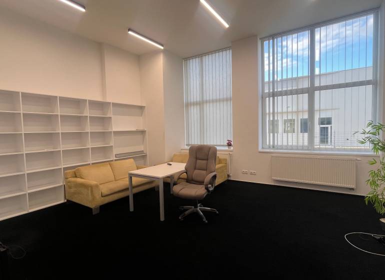 Irodák fekete szőnyeggel, bútorokkal, polcrendszerekkel és nagy ablakokkal.