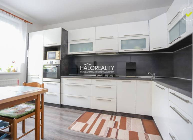 Konyha egy háromszobás lakásban fehér szekrényekkel és fa mintázatú padlóval.