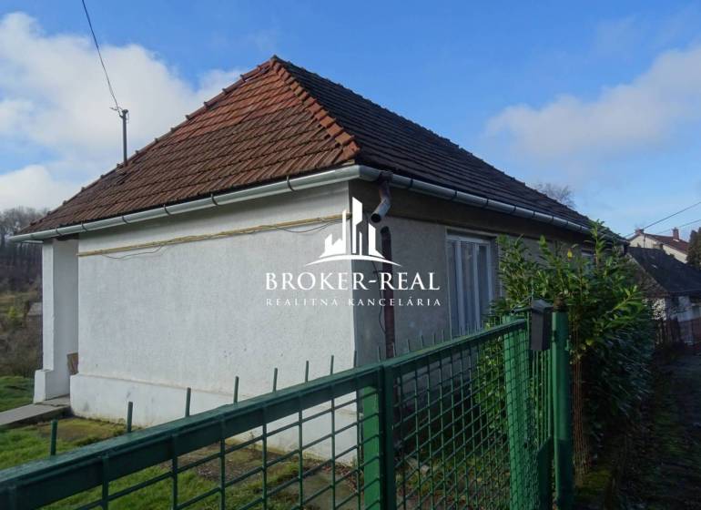Fehér homlokzatú és ferde tetős családi ház Rudabányán, zöld kerítés mögött.