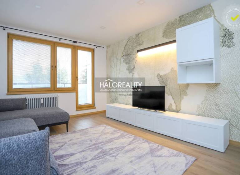 Világos nappali egy kétszobás lakásban kényelmes kanapéval és fa mintázatú padlóval.