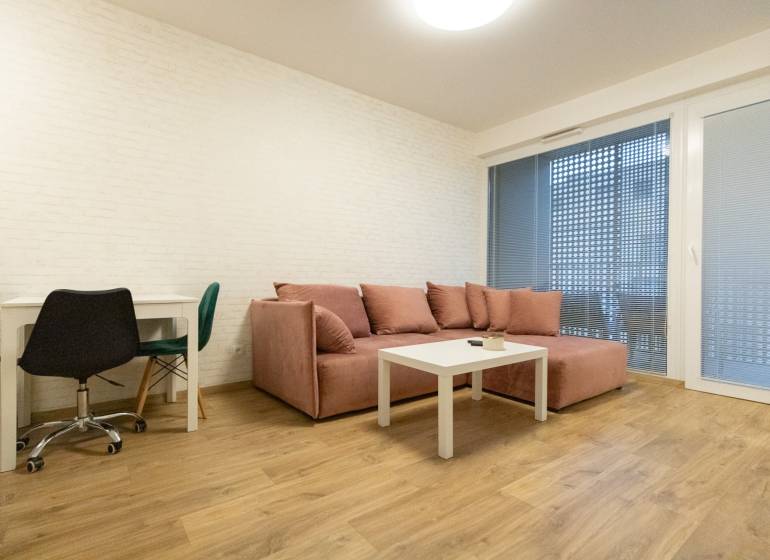 Nappali egy kétszobás lakásban kanapéval, asztallal és fa dekorációjú padlóval.