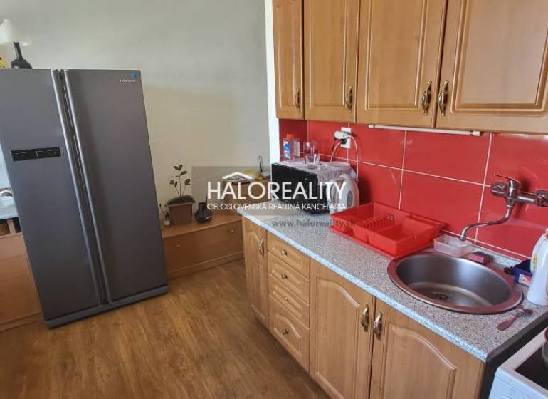 Konyha egy egyszobás lakásban fa szekrényekkel, piros csempékkel és nagy hűtőszekrénnyel.