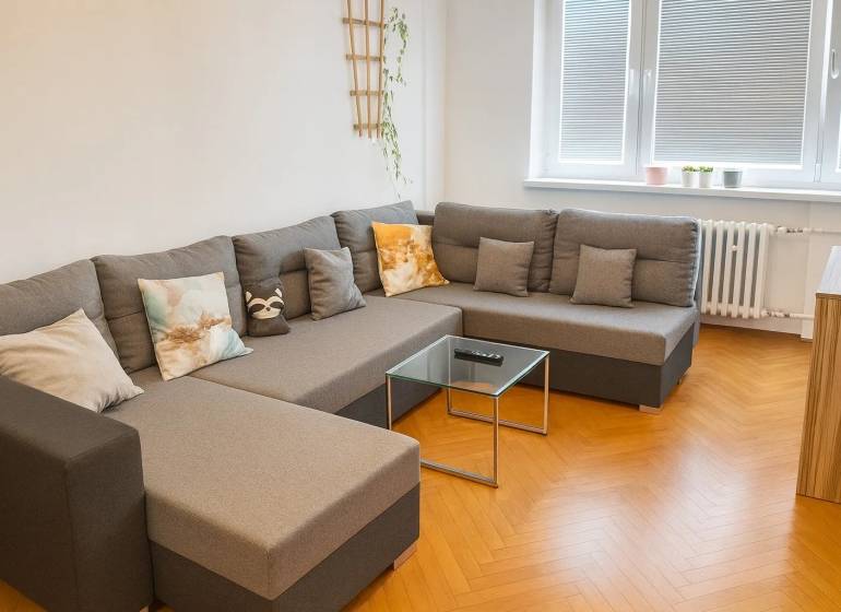 Nappali kényelmes kanapéval és fa mintázatú padlóval egy háromszobás lakásban.