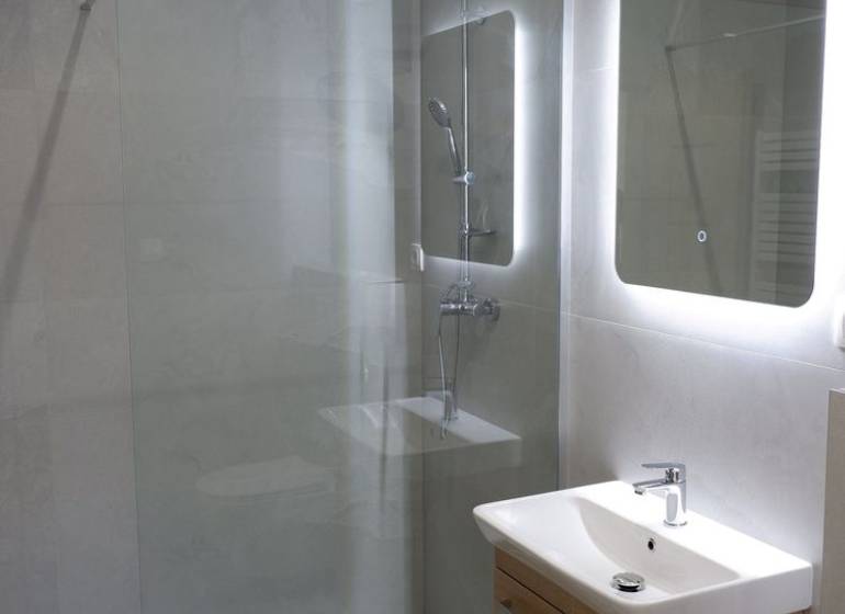Fürdőszoba mosdóval, zuhanyzóval és nagy tükörrel egy családi házban.
