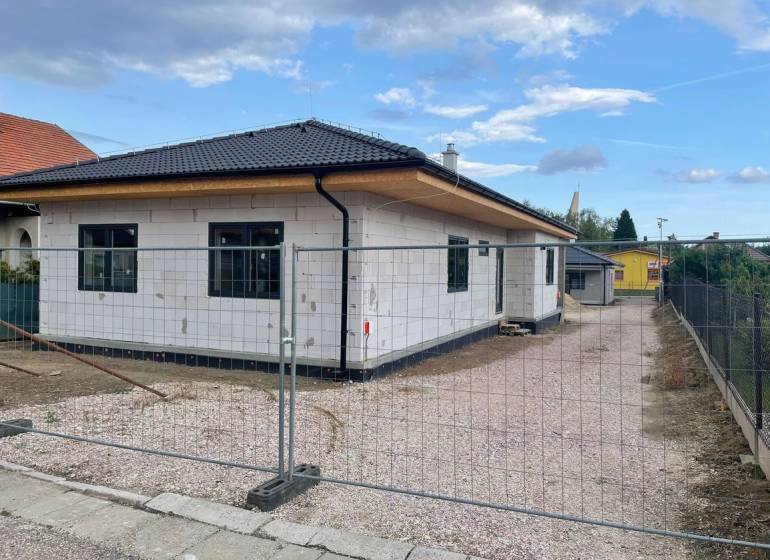 Radaván éppen épül egy családi ház ferde tetővel és fehér homlokzattal.