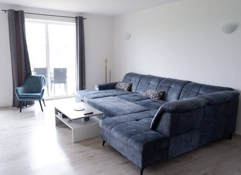 Nappali kék kanapéval és fotellel, fa mintázatú padlóval, családi ház.