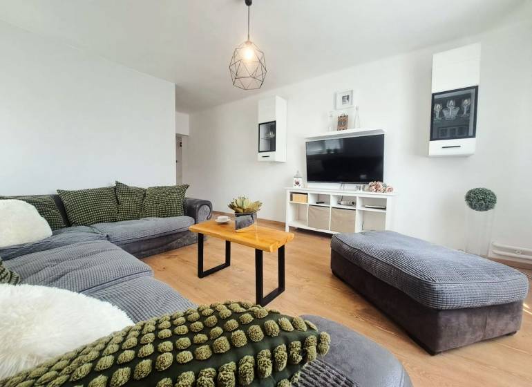 Nappali egy családi házban, fa mintázatú padlóval és kényelmes ülőgarnitúrával.