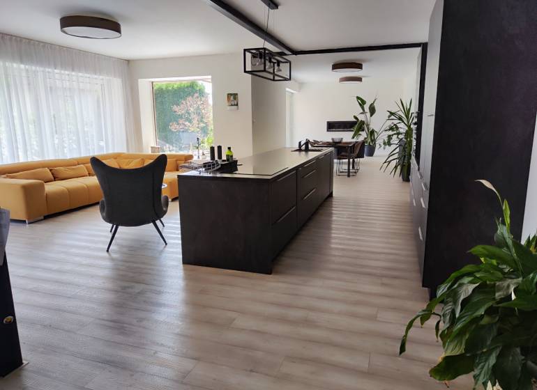 Konyha és nappali családi házban szigettel, sárga kanapéval és fa mintás padlóval.