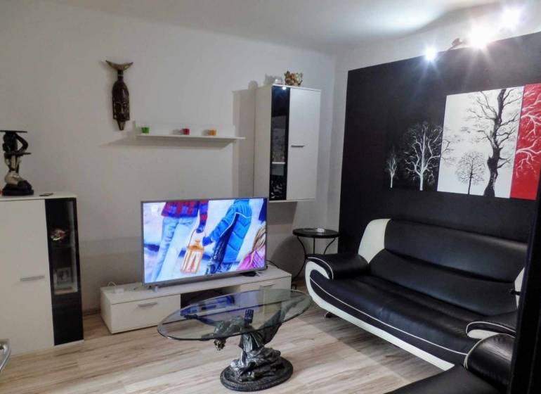 Nappali fekete-fehér kanapéval, fa mintázatú padlóval és televízióval.