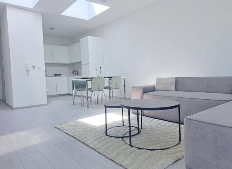 Világos nappali konyhával, kanapéval és fa dekoros padlóval egy kétszobás lakásban.