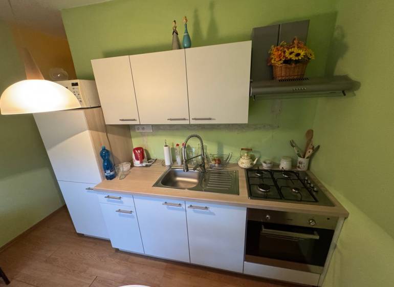 Konyha egy egyszobás lakásban fehér szekrényekkel és fa dekorációjú padlóval.