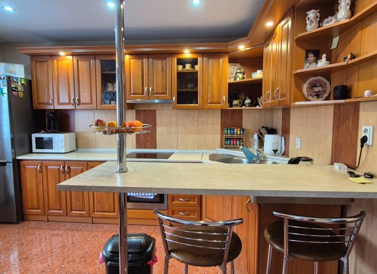 Konyha egy családi házban fa szekrényekkel, bárpulttal és háztartási gépekkel.