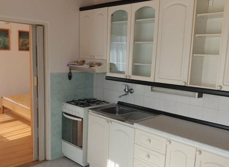 Konyha egy egyszobás lakásban fehér szekrényekkel, tűzhellyel és fa dekoros padlóval.