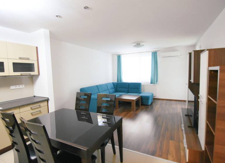 Nappali kék kanapéval, konyhával és fa dekoros padlóval egy kétszobás lakásban.