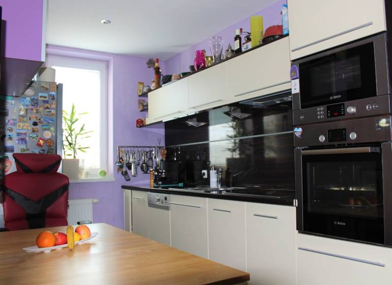 Konyha egy egyszobás lakásban világos szekrénnyel, székkel és gyümölcsökkel az asztalon.