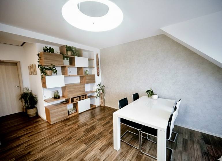 Étkezőasztal, székek és polcok dekorációs elemekkel egy háromszobás lakásban, fa dekoros padlóval.